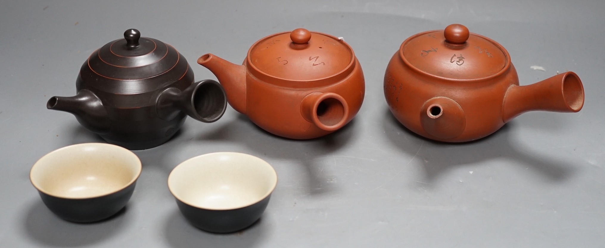 Two Japanese redware teapots, a similar brown stoneware teapot and two cups